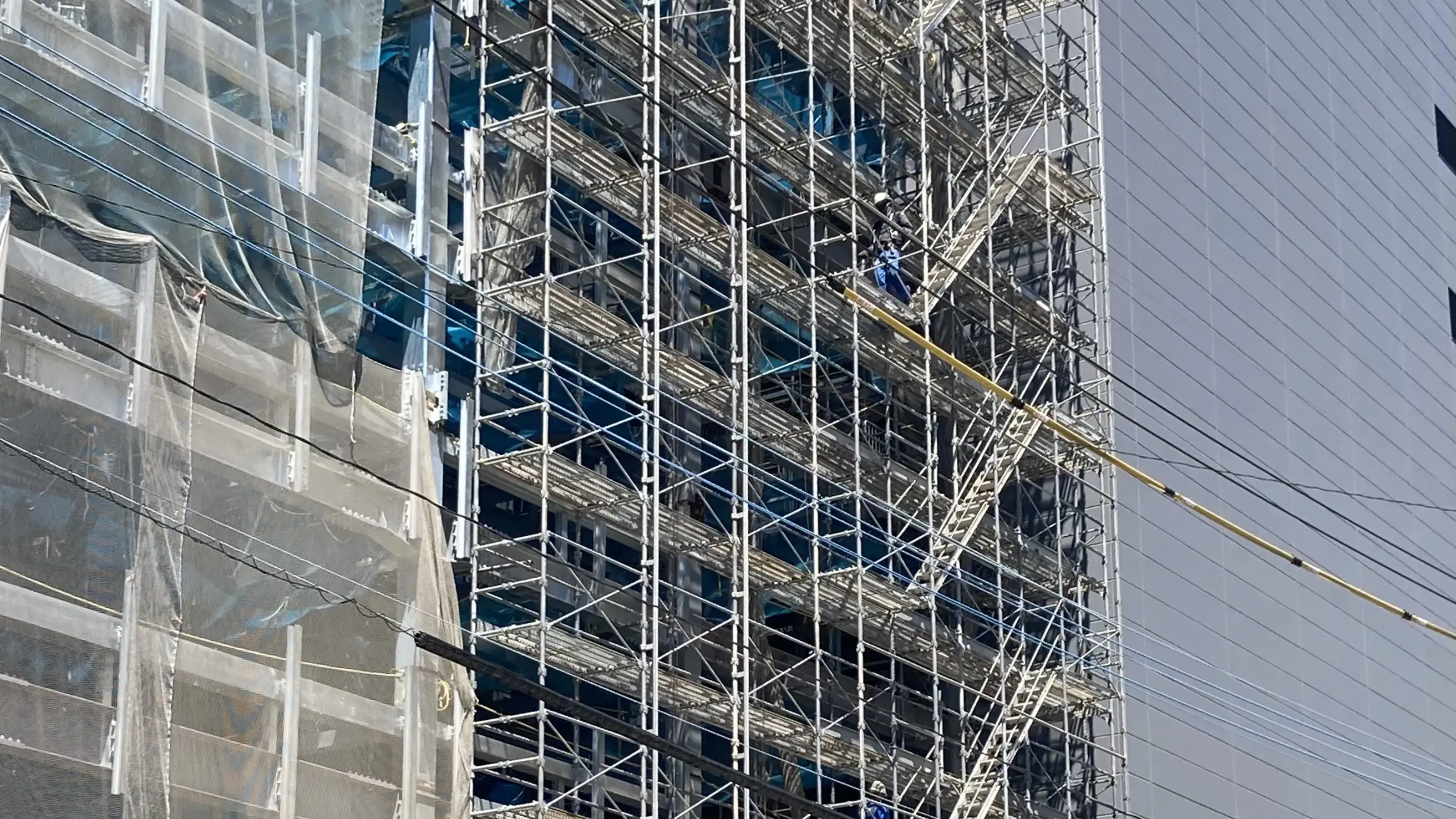 高層建物の外壁改修工事で設置されたくさび式足場と作業員の安全作業状況