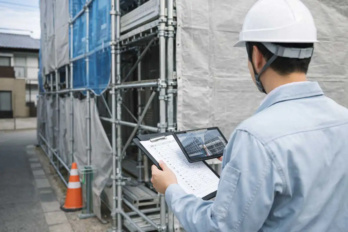 足場現場で現場監督がチェックリストとタブレットを使って点検と記録を行っている様子