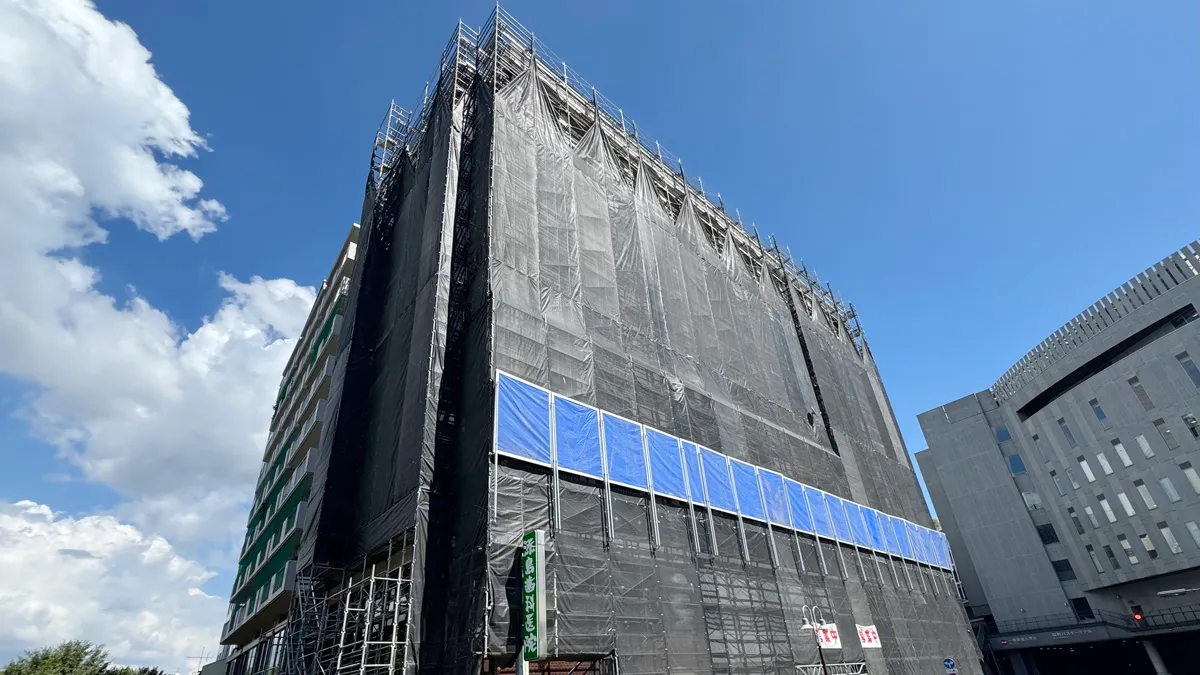 高層建物を覆うくさび式足場とメッシュシート。改修工事中の現場を撮影した実写真。