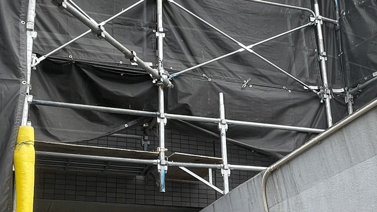 クサビ式足場を建物外壁に設置した現場写真|黒い養生シートと壁つなぎ金具が確認できる安全施工例