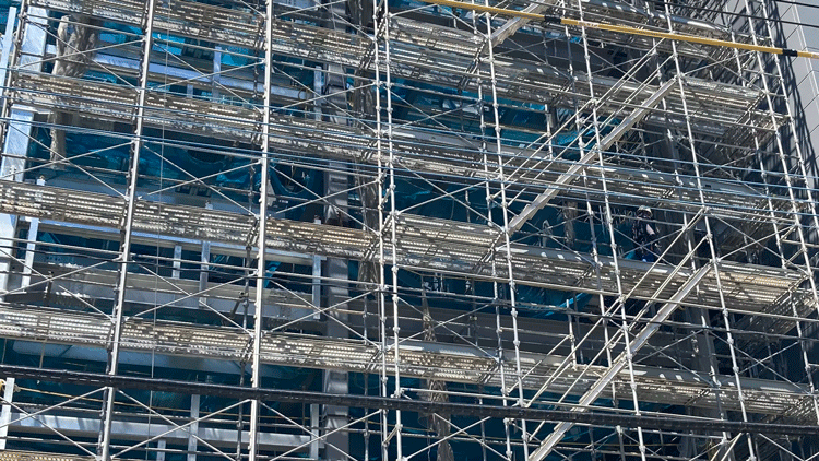 クサビ緊結式足場の外観。建設中のビル外壁に組まれた足場が整然と組み上げられ、安全手すりと筋交いが確認できる。