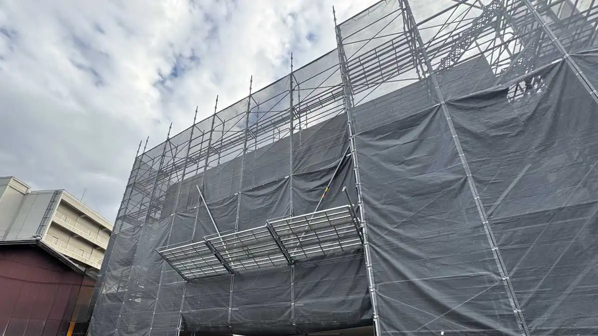 養生シートで覆われた建物外周の外部足場と張り出しブラケット。枠組足場とクサビ足場のコスパと安全性を比較する現場イメージ